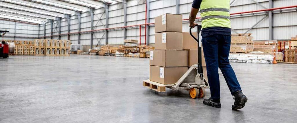 A warehouse worker moving a pallet of freight on a pallet jack