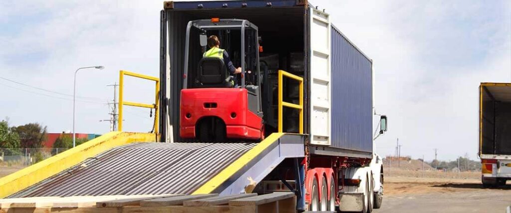 A forklift drives into the back of a semi truck for loading