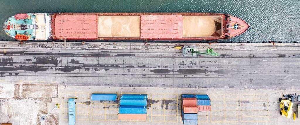Aerial view of a dry bulk barge at dock with containers nearby
